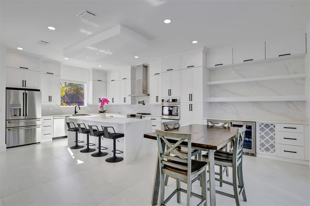 A modern white kitchen features a large island with bar stools and a dining table — 3723 NORWOOD COURT, SARASOTA, FL