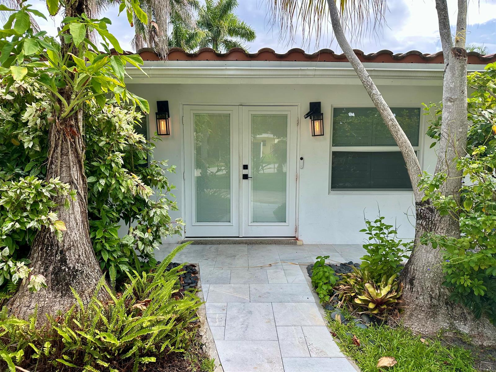 A white house exterior features double glass doors, two black wall sconces, and a stone walkway — 212 Kings Lynn, Delray Beach FL 33444, DELRAY BEACH, FL