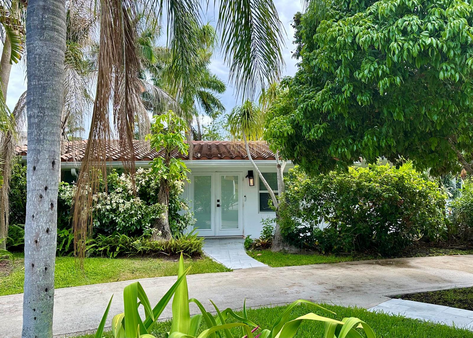 A white house with a tiled roof and glass double doors surrounded by lush landscaping — 212 Kings Lynn, Delray Beach FL 33444, DELRAY BEACH, FL