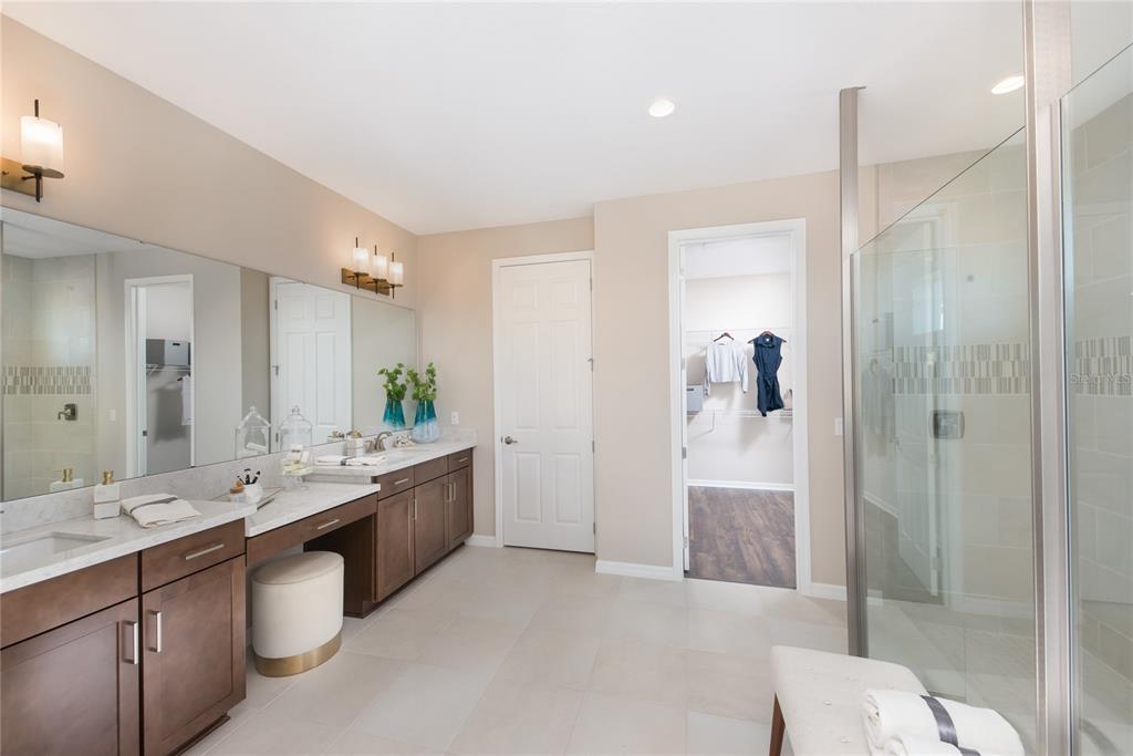 A bathroom features a double vanity with dark cabinets, a glass shower, and a walk-in closet — 16224 ALPHA GROVE PLACE, ODESSA, FL