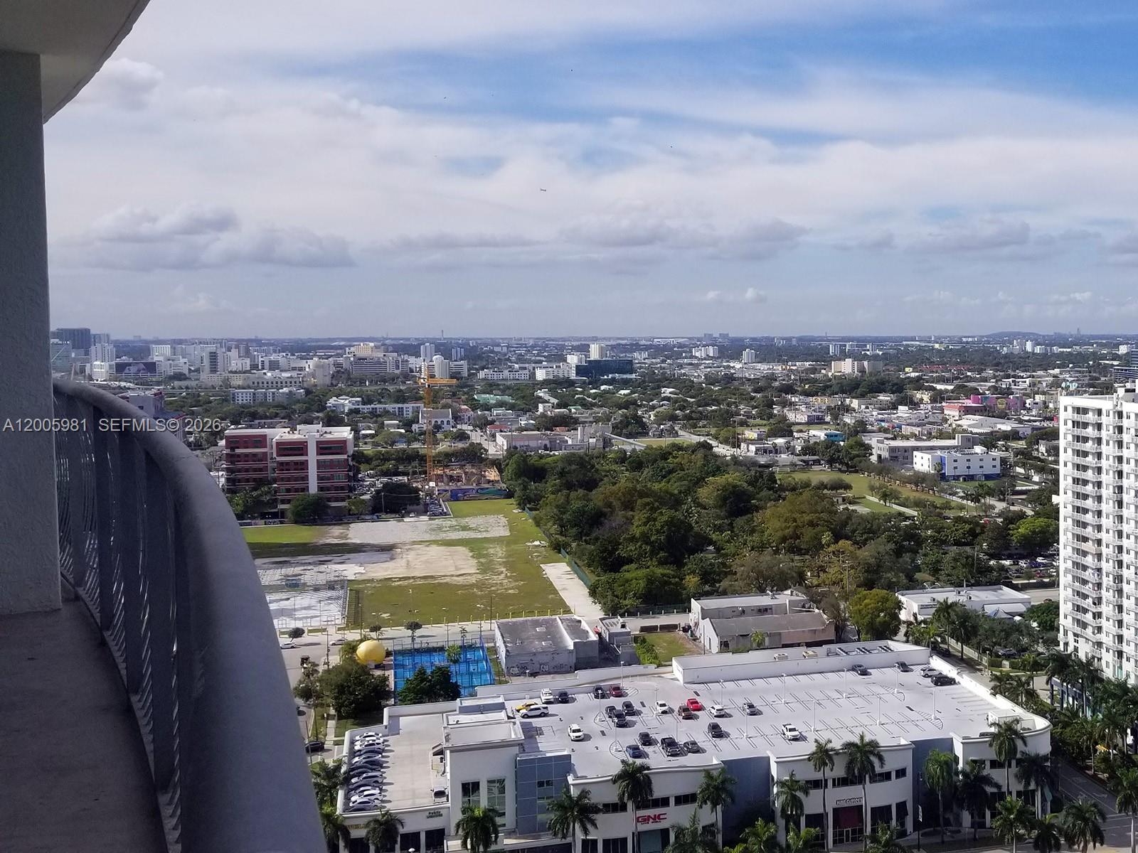 An elevated view from a balcony overlooking a city, parking lot, and green space — 1750 N BAYSHORE DR # 2909, Miami FL 33132, MIAMI, FL