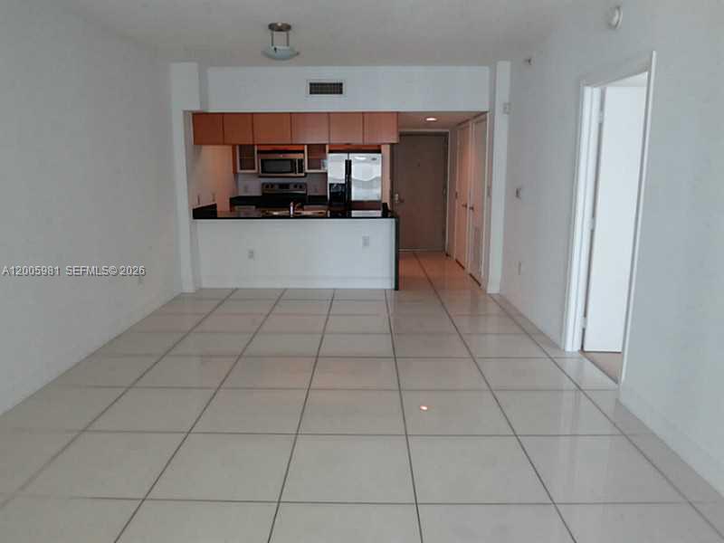 An open-concept kitchen with wood cabinets and white tile floors overlooks a living area — 1750 N BAYSHORE DR # 2909, Miami FL 33132, MIAMI, FL