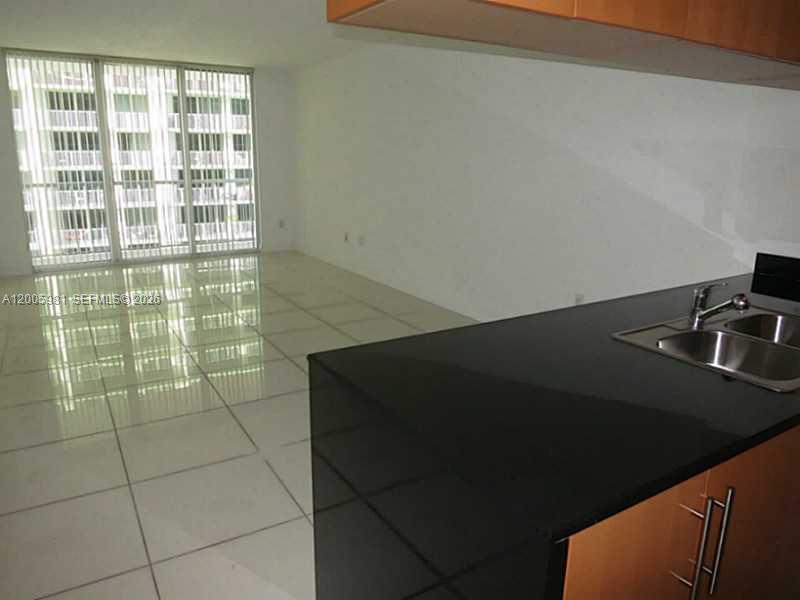 A kitchen with a black countertop and sink overlooks an empty room with tiled floors — 1750 N BAYSHORE DR # 2909, Miami FL 33132, MIAMI, FL