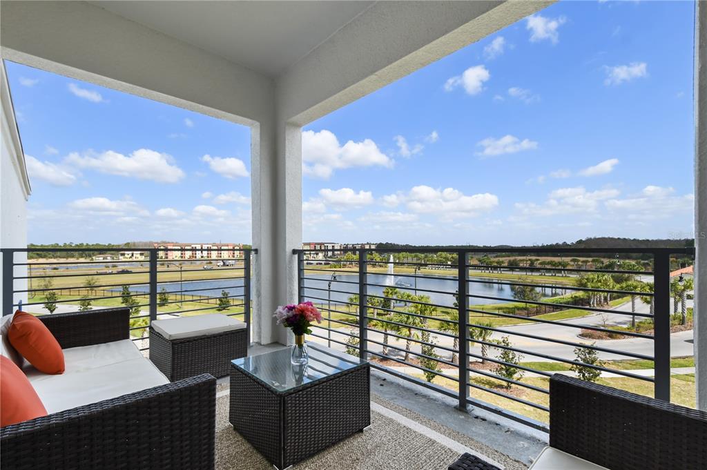 A covered balcony features wicker patio furniture overlooking a lake with a fountain — 3191 PARADOX CIRCLE UNIT 401, KISSIMMEE, FL