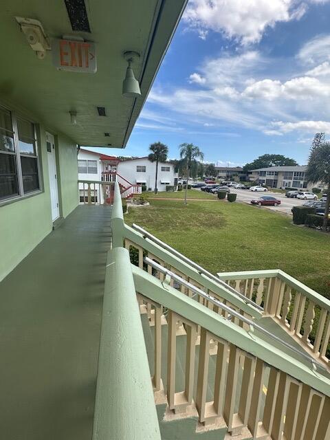 An outdoor walkway with green flooring leads to a staircase overlooking a parking lot — 72 Norwich C, West Palm Beach FL 33417, WEST PALM BEACH, FL