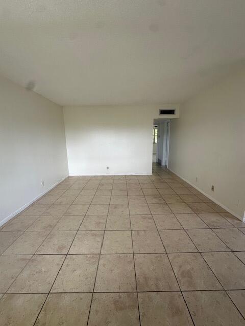 An empty room with beige tile flooring and white walls leads to a doorway — 72 Norwich C, West Palm Beach FL 33417, WEST PALM BEACH, FL