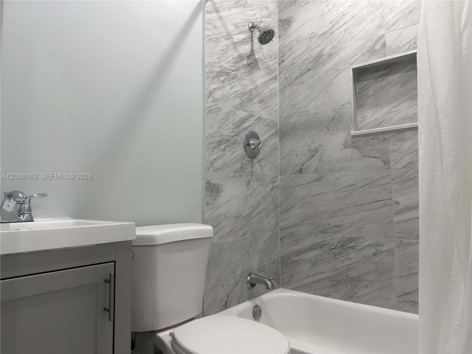 A bathroom features a gray vanity, a white toilet, and a marble-tiled shower-tub combination — 214 SW 2nd Ter, Dania Beach FL 33004, DANIA BEACH, FL