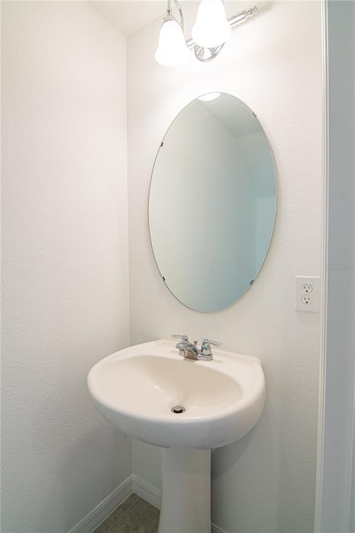 A white pedestal sink with a chrome faucet sits below an oval mirror and light — 205 MANDOVI STREET, DAVENPORT, FL