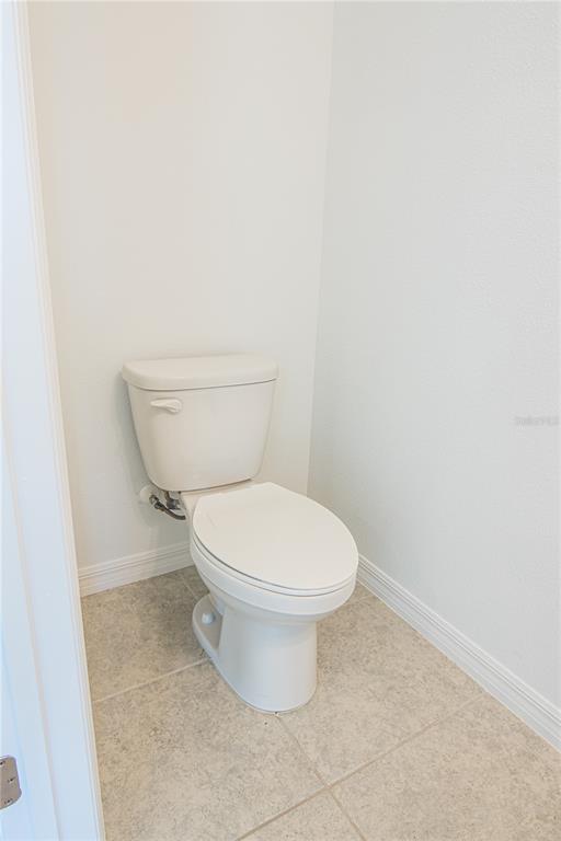A white toilet is positioned in the corner of a room with tiled flooring — 205 MANDOVI STREET, DAVENPORT, FL