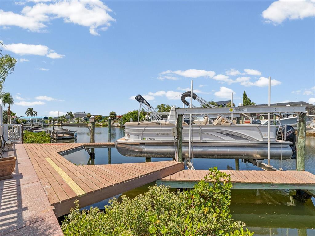 A pontoon boat sits on a lift at a wooden dock along a canal — 15709 CENTURY DRIVE, HUDSON, FL