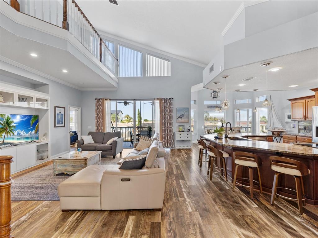 An open-concept living room and kitchen featuring vaulted ceilings, wood flooring, and a breakfast bar — 15709 CENTURY DRIVE, HUDSON, FL