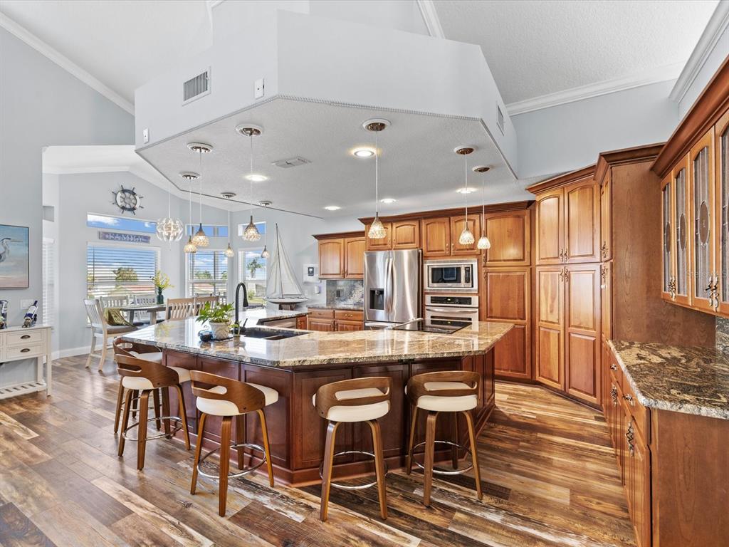 A kitchen features a large granite-topped island, wooden cabinetry, and four bar stools — 15709 CENTURY DRIVE, HUDSON, FL