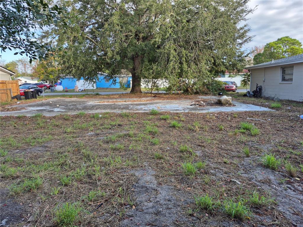 A large concrete slab sits in a yard with a large tree and neighboring houses — 7116 DIPAOLA DRIVE, HUDSON, FL