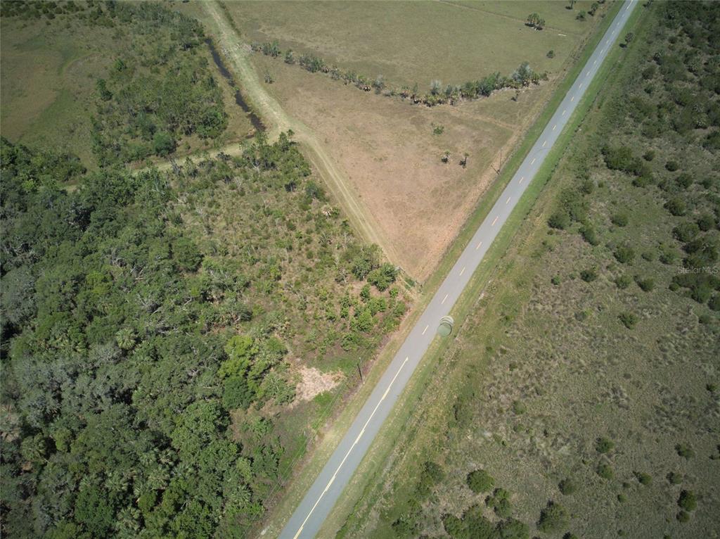 An aerial view shows a paved road running diagonally through a rural, wooded landscape — EMERALDA ISLAND ROAD, LEESBURG, FL