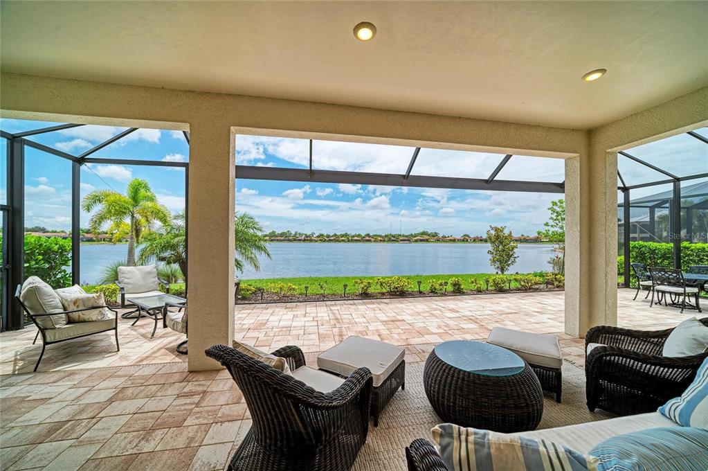A covered patio with wicker furniture overlooks a lake through a screened-in enclosure — 289 VILLORESI BOULEVARD, NOKOMIS, FL