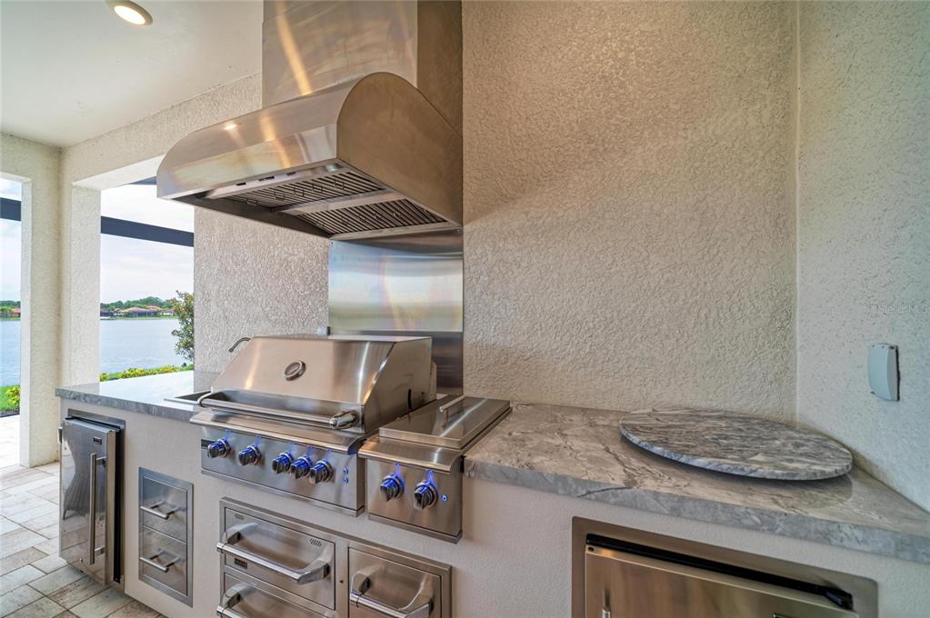 An outdoor kitchen features stainless steel appliances, a marble countertop, and a view of water — 289 VILLORESI BOULEVARD, NOKOMIS, FL