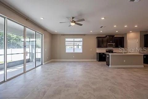 An open-concept living area features tile flooring, a ceiling fan, and an adjacent kitchen — 4444 DESERT ROSE AVENUE, KISSIMMEE, FL