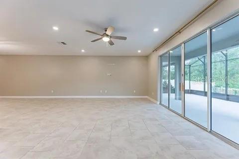 An empty living room features light-colored tile flooring, a ceiling fan, and large sliding glass doors — 4444 DESERT ROSE AVENUE, KISSIMMEE, FL