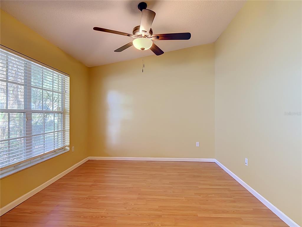 An empty room features light-colored walls, wood-look flooring, a ceiling fan, and a large window — 166 BUCKHORN RUN, LAKELAND, FL