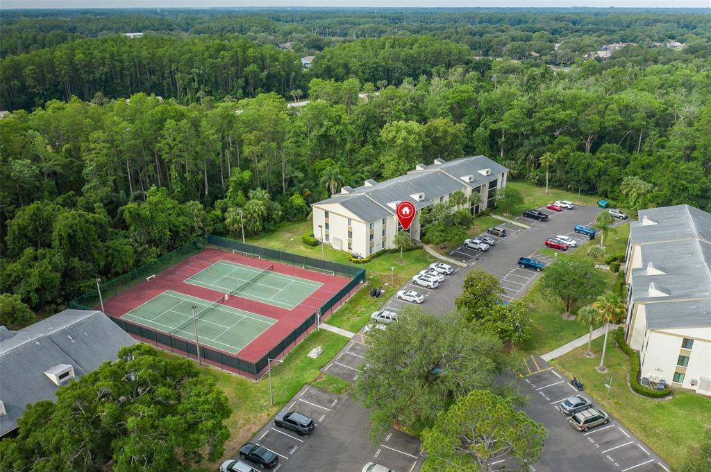 An aerial view shows apartment buildings, a tennis court, and a parking lot — 3166 LAKE PINE WAY S UNIT A2, TARPON SPRINGS, FL