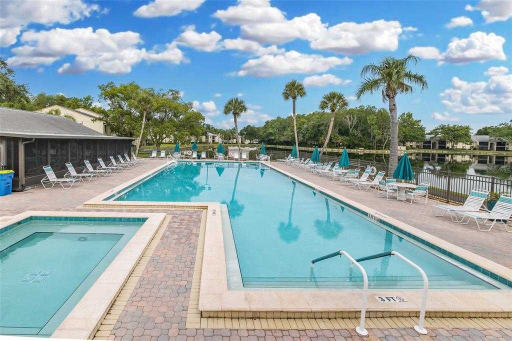 A rectangular swimming pool and attached hot tub sit on a paved deck by a lake — 3166 LAKE PINE WAY S UNIT A2, TARPON SPRINGS, FL