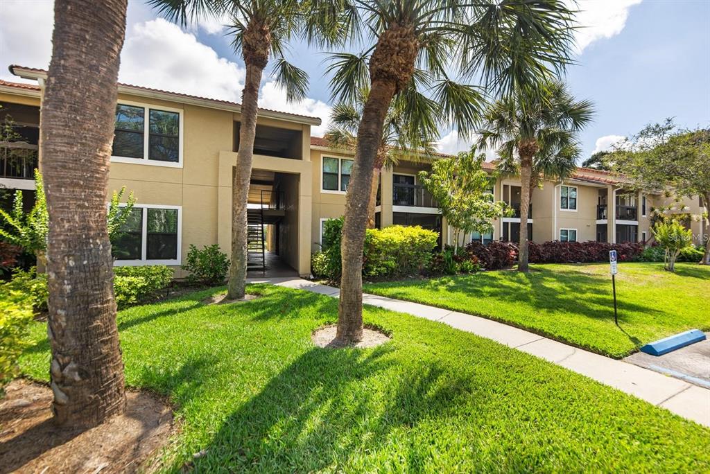 A multi-story apartment building with tan stucco walls, palm trees, and a paved walkway — 4045 CROCKERS LAKE BOULEVARD UNIT 11, SARASOTA, FL