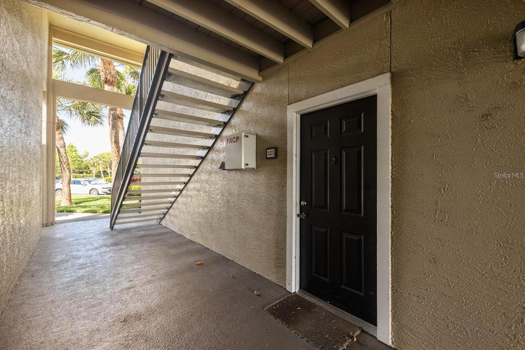 A black front door sits next to an outdoor staircase and a fire alarm control panel — 4045 CROCKERS LAKE BOULEVARD UNIT 11, SARASOTA, FL