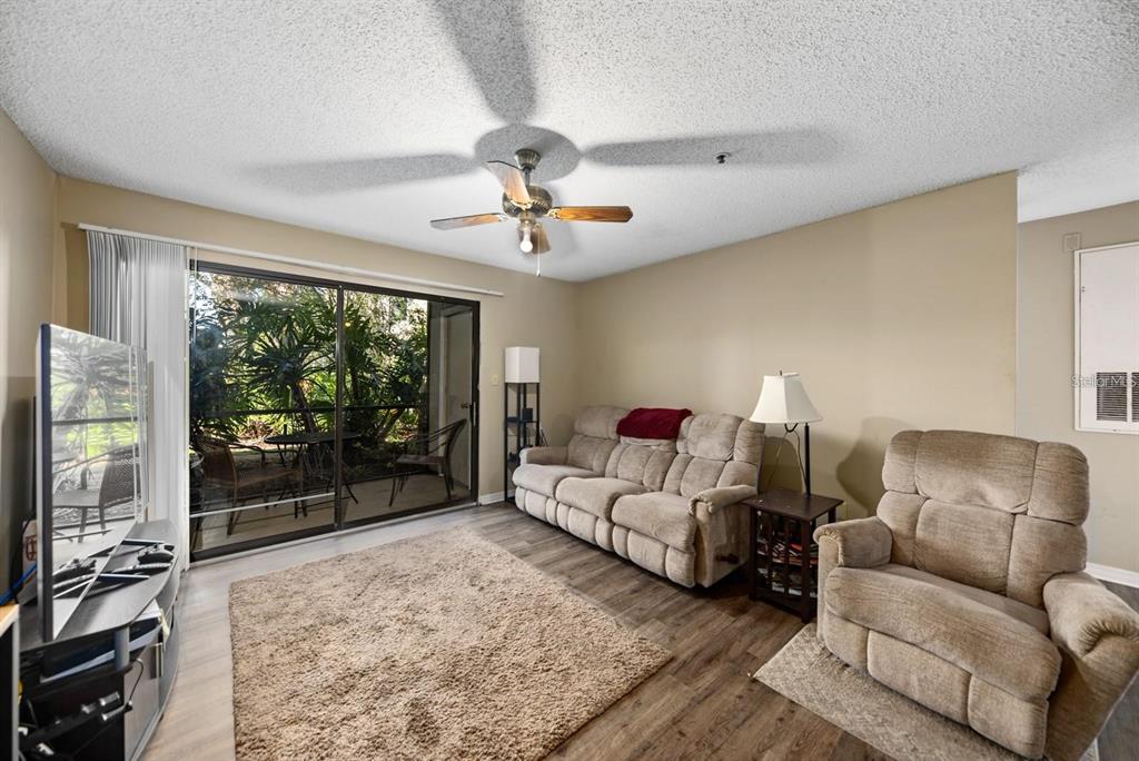 A living room with wood-look flooring, a beige sofa, a recliner, and a sliding glass door — 4045 CROCKERS LAKE BOULEVARD UNIT 11, SARASOTA, FL