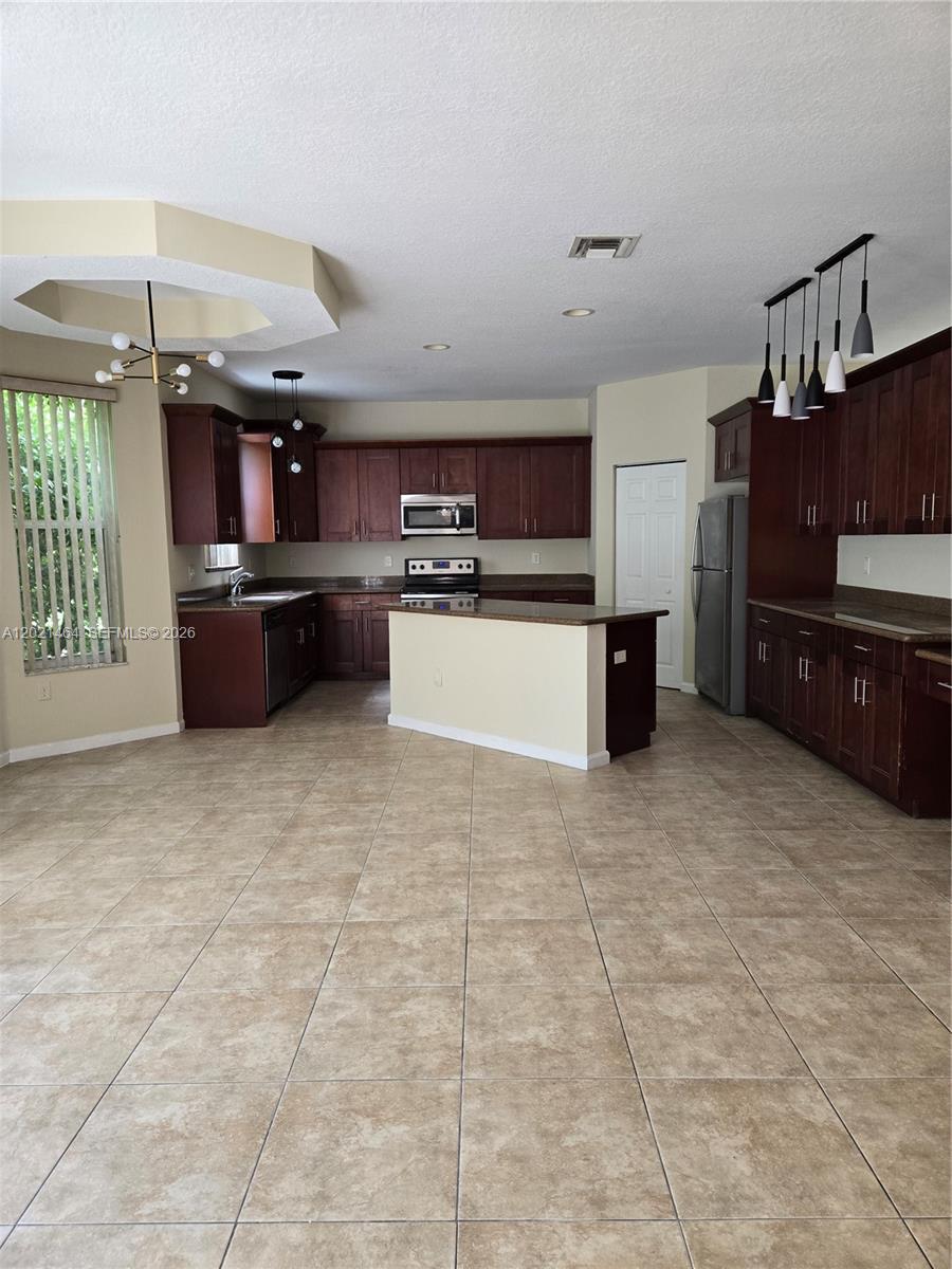 A kitchen with dark wood cabinets, a central island, and beige tile flooring — 2221 Sloane Pl, Wellington FL 33414, WELLINGTON, FL