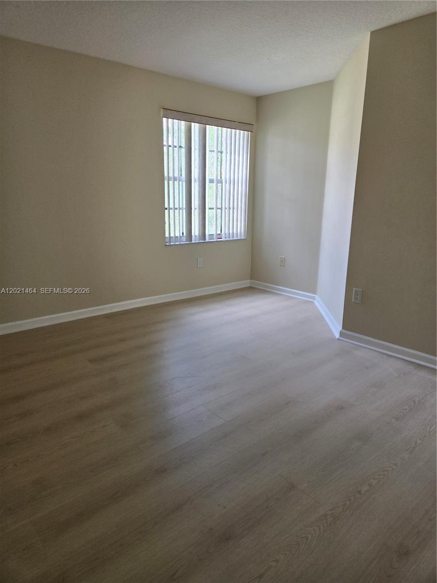 An empty room features light-colored wood-look flooring, beige walls, and a window with vertical blinds — 2221 Sloane Pl, Wellington FL 33414, WELLINGTON, FL