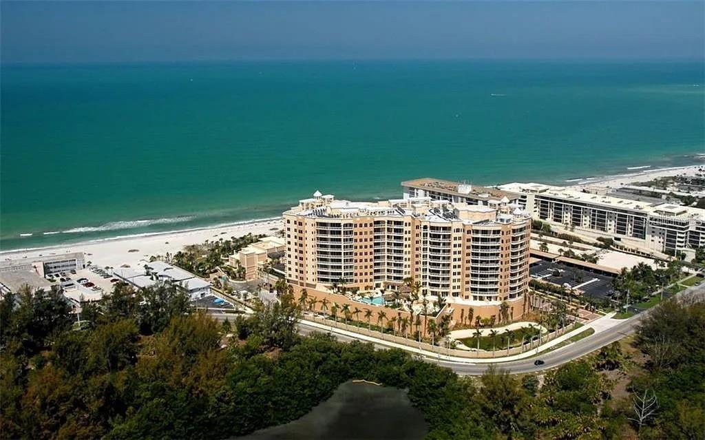 An aerial view shows a large beachfront condominium complex surrounded by trees and the ocean — 1111 RITZ CARLTON DRIVE UNIT 1004, SARASOTA, FL