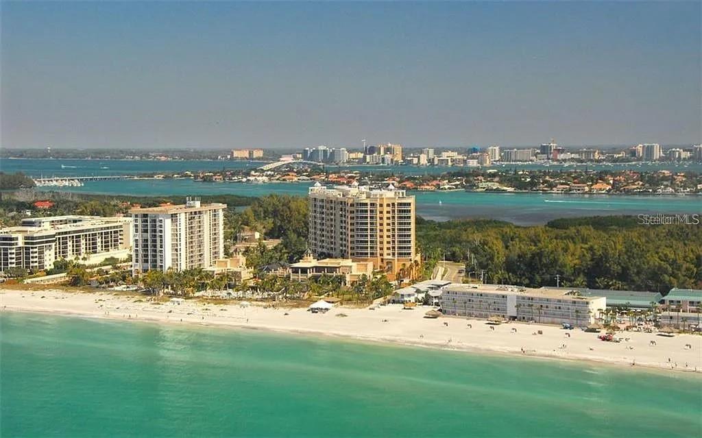 An aerial view of a sandy beach with high-rise buildings and a distant city skyline — 1111 RITZ CARLTON DRIVE UNIT 1004, SARASOTA, FL