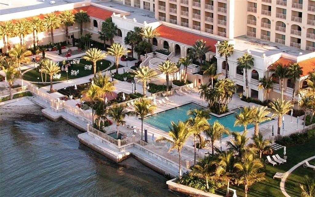 An aerial view of a resort pool area with palm trees adjacent to a waterfront — 1111 RITZ CARLTON DRIVE UNIT 1004, SARASOTA, FL