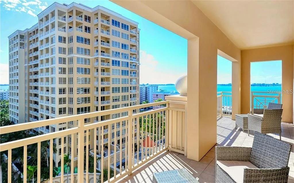 A balcony with wicker chairs overlooks a tall apartment building and a body of water — 1111 RITZ CARLTON DRIVE UNIT 1004, SARASOTA, FL