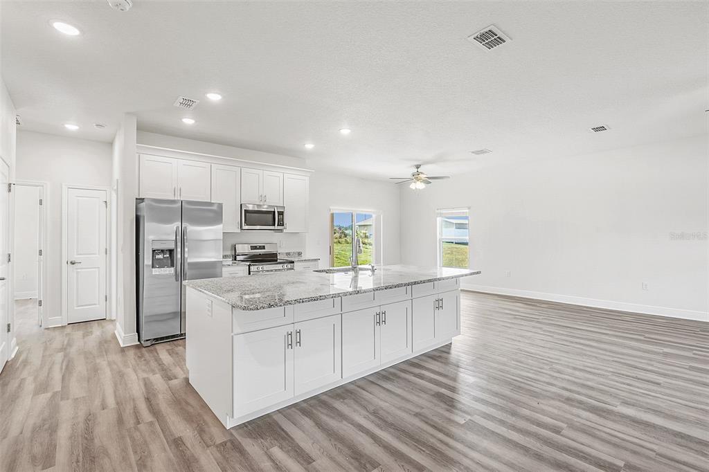 A modern kitchen features white cabinets, granite countertops, a large island, and light wood flooring — 44 W LYNNHAVEN PLACE, CITRUS SPRINGS, FL