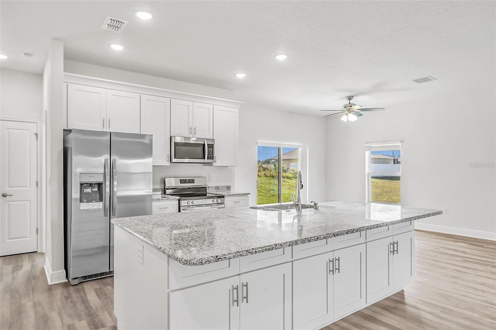 A modern kitchen features white cabinetry, stainless steel appliances, and a large granite-topped island — 44 W LYNNHAVEN PLACE, CITRUS SPRINGS, FL