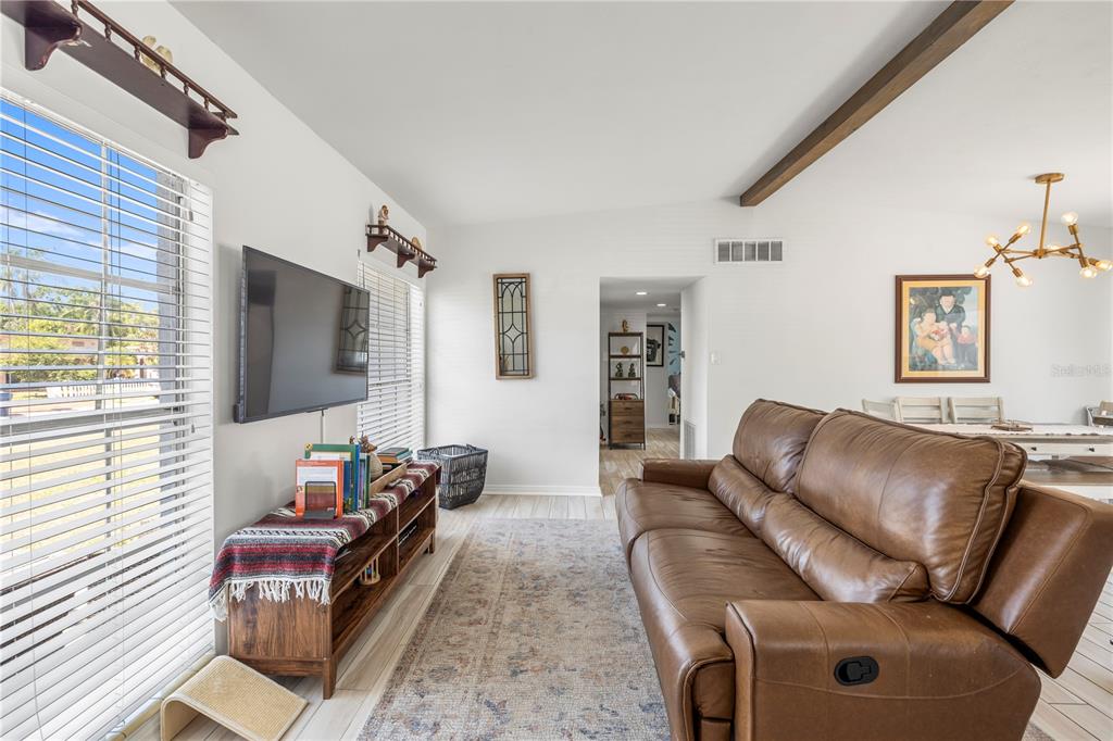 An empty room features wood-look tile flooring, white walls, a wooden ceiling beam, and windows — 2125 W HIAWATHA STREET, TAMPA, FL
