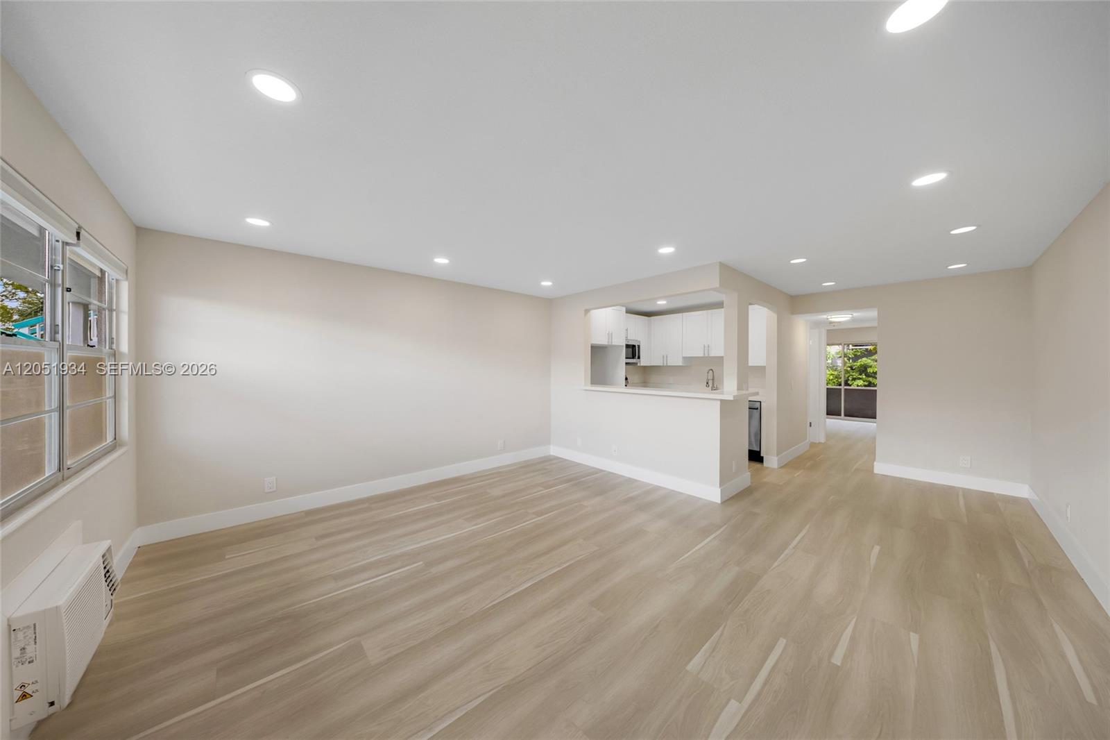 An empty living room features light wood-look flooring, recessed lighting, and a pass-through kitchen window — 130 Ventnor I # 130, Deerfield Beach FL 33442, DEERFIELD BEACH, FL