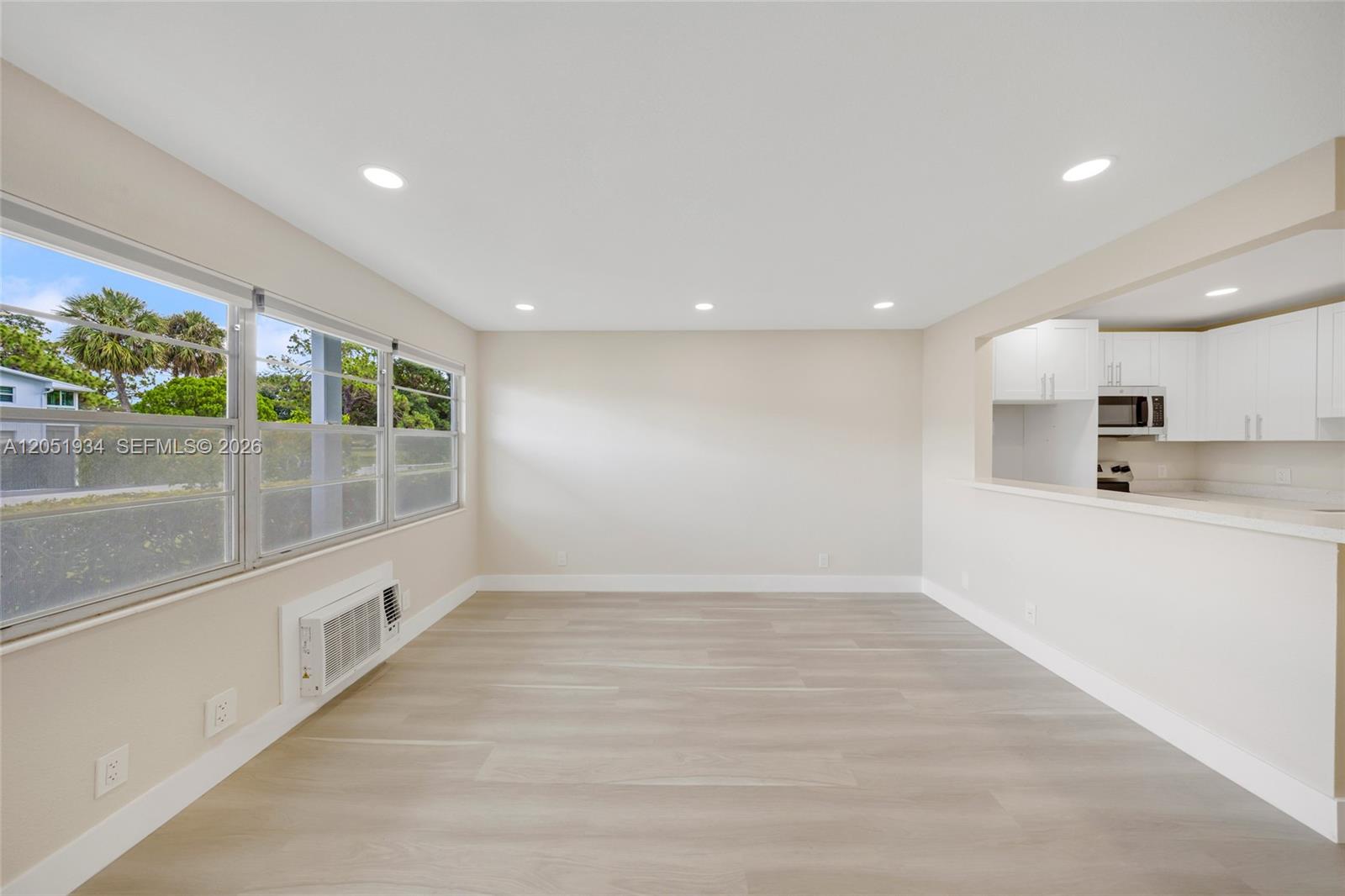 An empty room with light wood-look flooring, recessed lighting, and a view into a kitchen — 130 Ventnor I # 130, Deerfield Beach FL 33442, DEERFIELD BEACH, FL