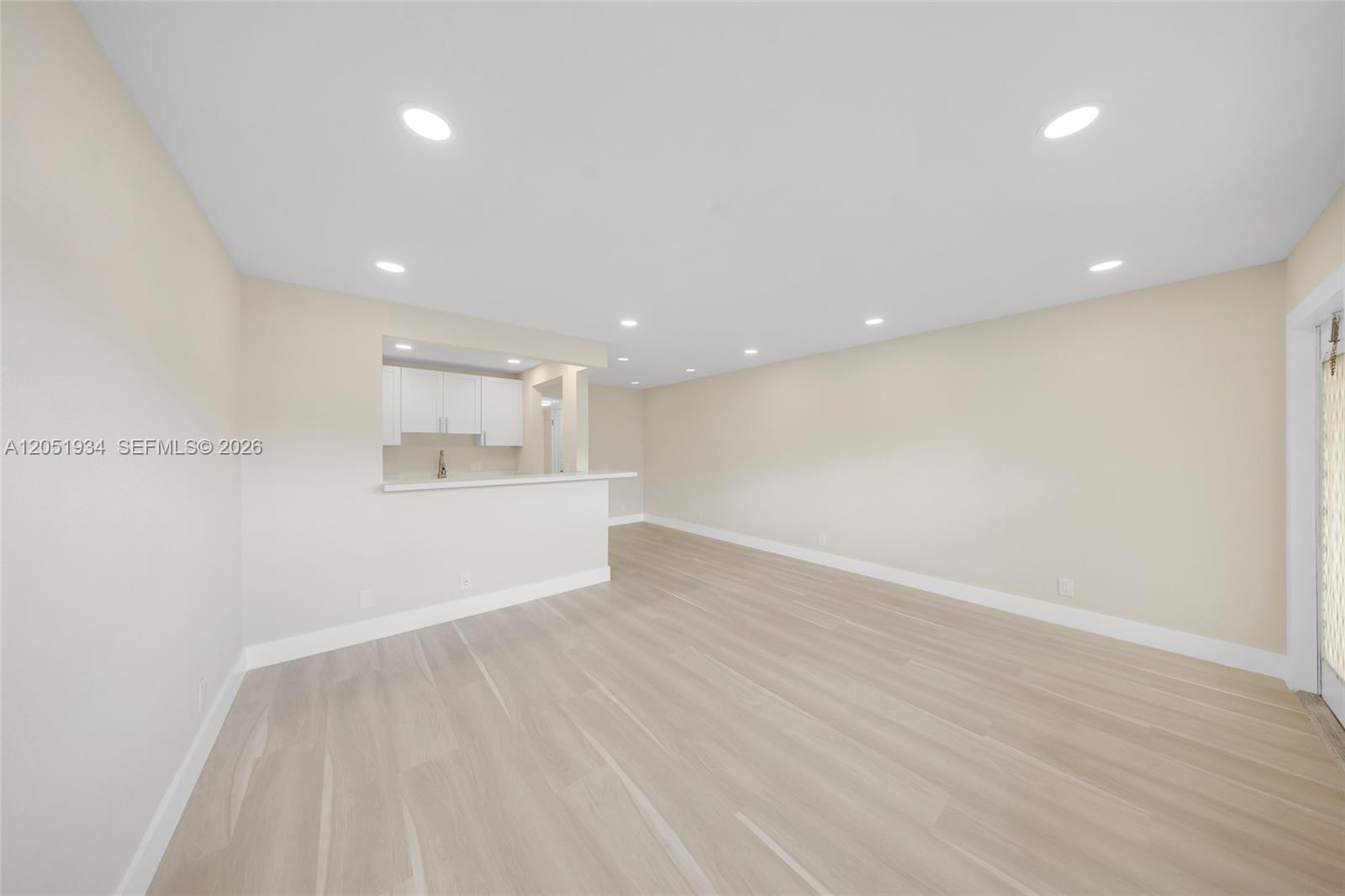 An empty living room features light-colored wood flooring, recessed lighting, and a kitchen pass-through window — 130 Ventnor I # 130, Deerfield Beach FL 33442, DEERFIELD BEACH, FL