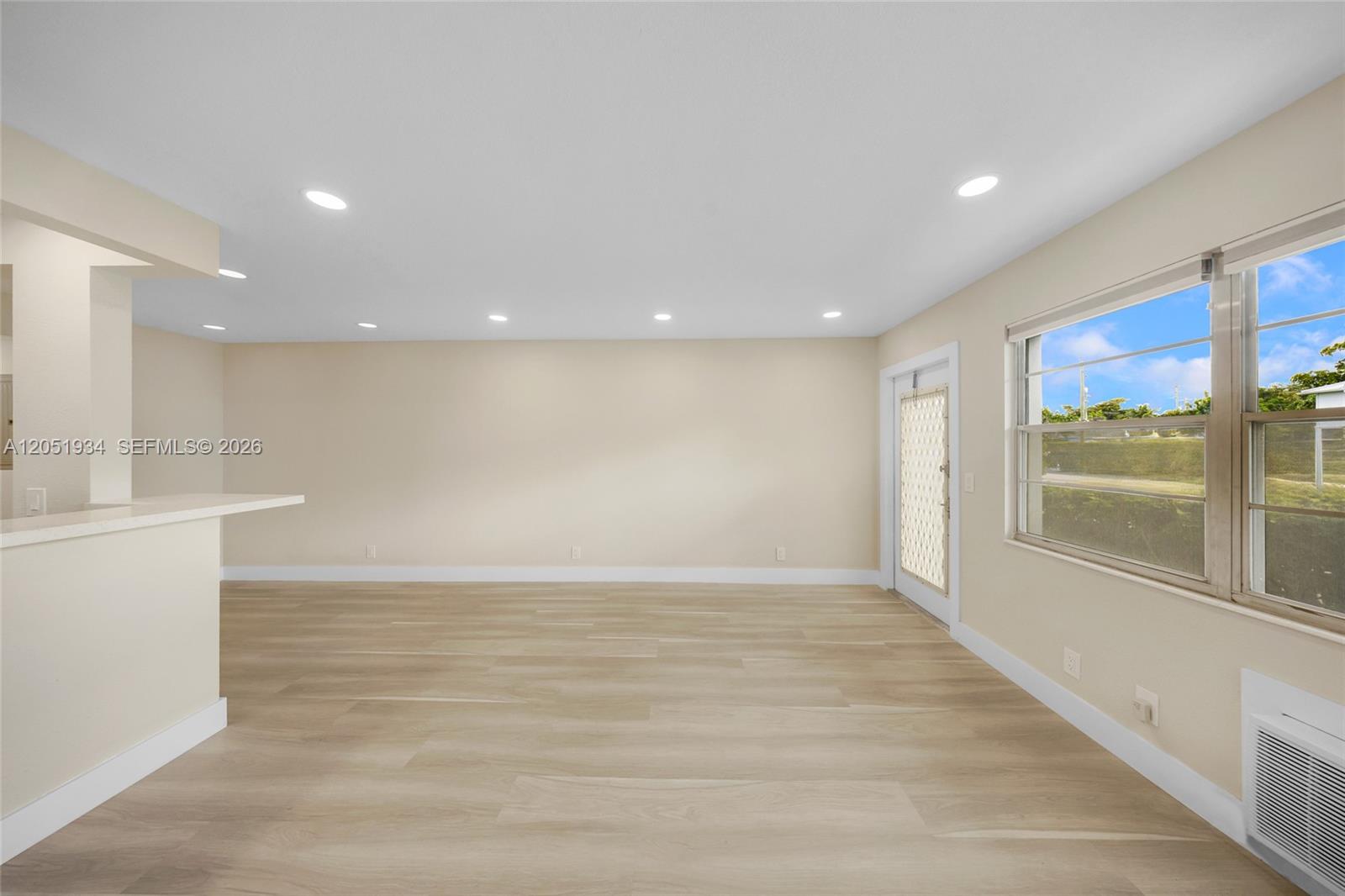 An empty room features light wood-look flooring, recessed lighting, a breakfast bar, and a window — 130 Ventnor I # 130, Deerfield Beach FL 33442, DEERFIELD BEACH, FL