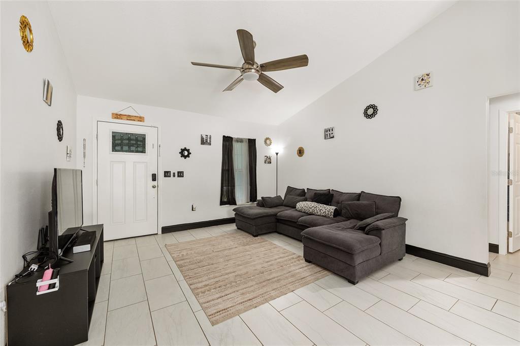 A living room features white walls, tile flooring, a gray sectional sofa, and a ceiling fan — 3781 SE 144TH LANE, SUMMERFIELD, FL