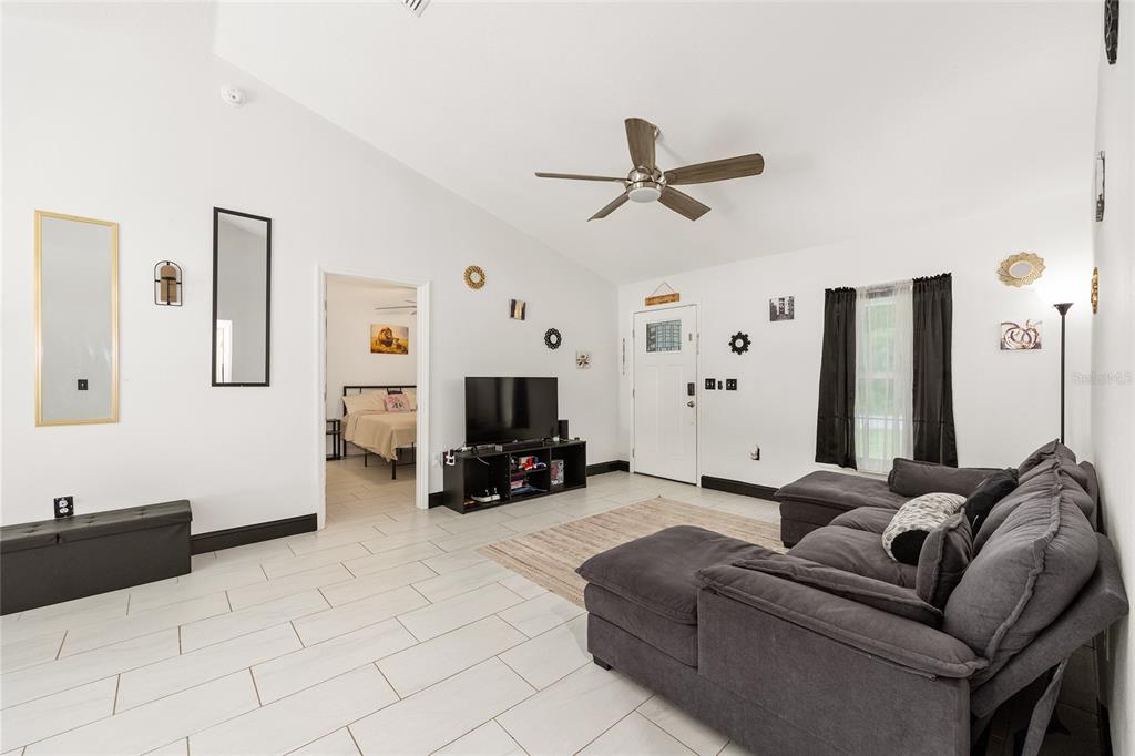 A living room with white walls, tile flooring, a gray sectional sofa, and a television — 3781 SE 144TH LANE, SUMMERFIELD, FL