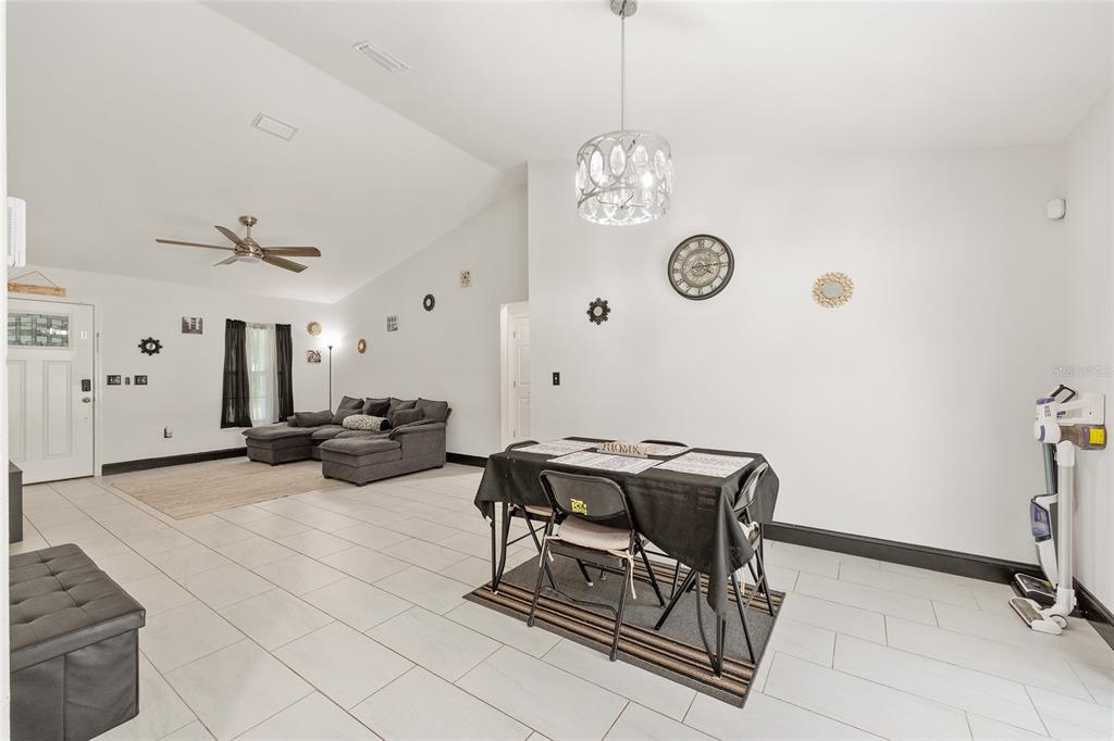 A living and dining area with white walls, tile flooring, and a vaulted ceiling — 3781 SE 144TH LANE, SUMMERFIELD, FL