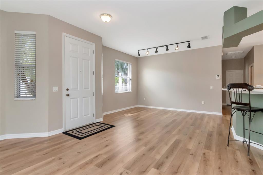 A living area features light wood-look flooring, beige walls, a white front door, and track lighting — 21433 DIAMONTE DRIVE, LAND O LAKES, FL