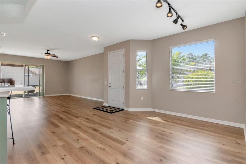 An open-concept living area features light wood-look flooring, a white front door, and large windows — 21433 DIAMONTE DRIVE, LAND O LAKES, FL
