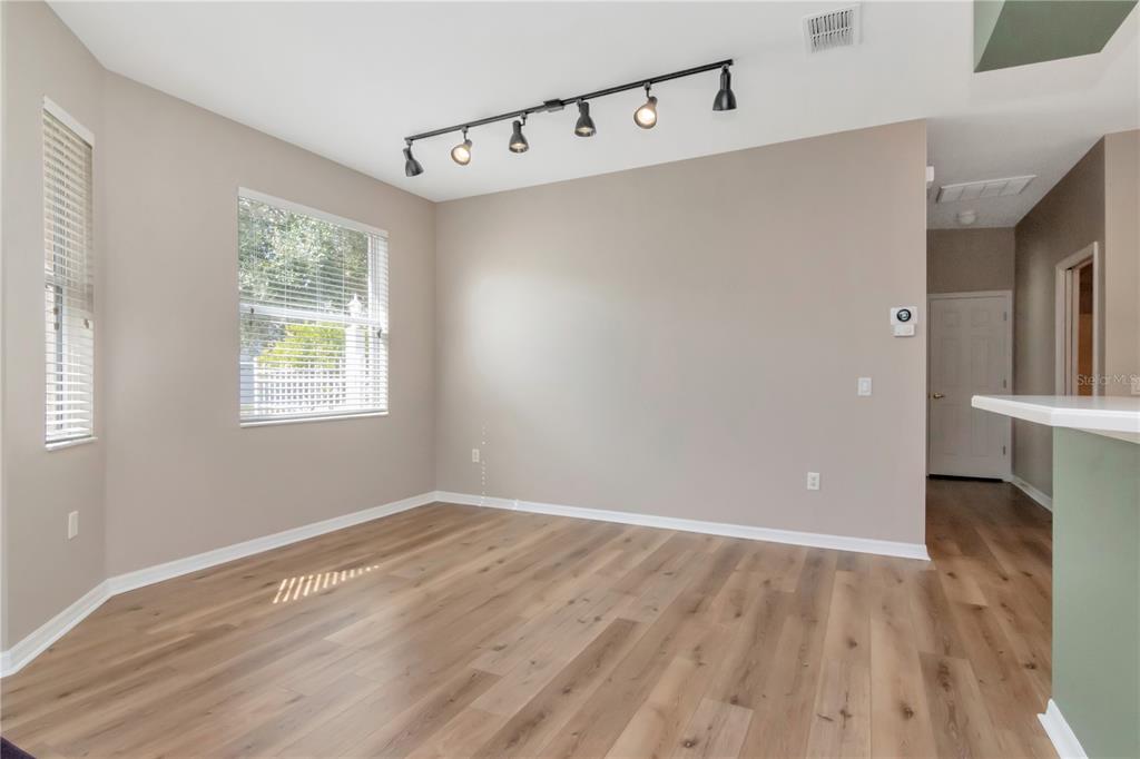 An empty dining area features light wood-look flooring, beige walls, and a track lighting fixture — 21433 DIAMONTE DRIVE, LAND O LAKES, FL