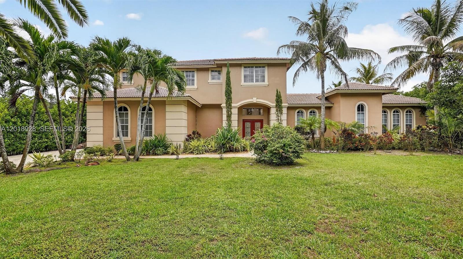 A two-story tan stucco house with a tiled roof and arched windows sits behind a lawn — 5960 NW 79th Way, Parkland FL 33067, PARKLAND, FL