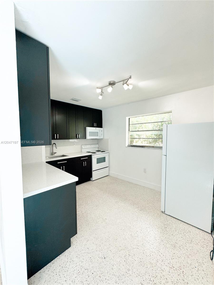 A kitchen features dark cabinets, white countertops, white appliances, and light-colored speckled flooring — MIAMI, FL
