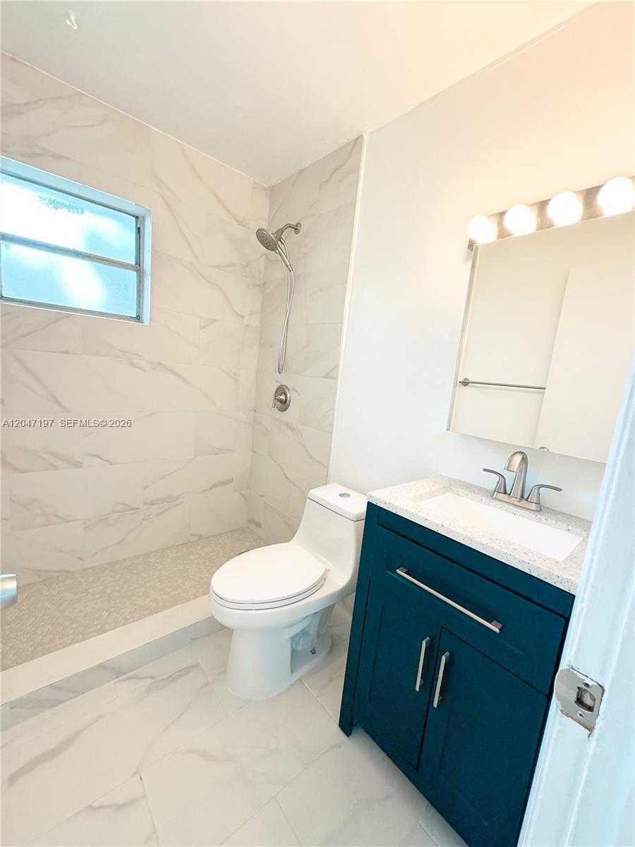 A bathroom features a walk-in shower with marble-look tile, a white toilet, and a blue vanity — MIAMI, FL